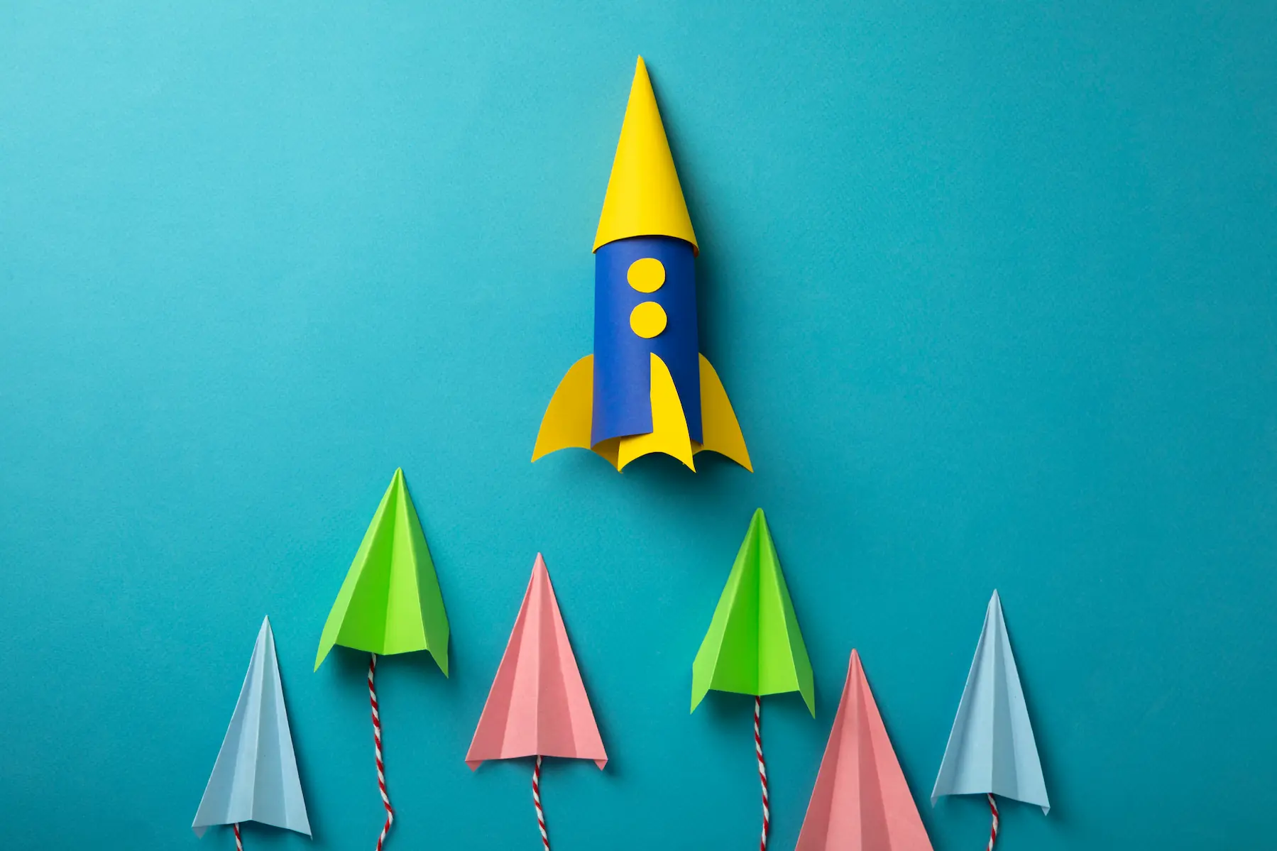 Une fusée en carton colorée sur fond bleu avec des petits avions en papier jute dessous qui s'envolent vers le haut
