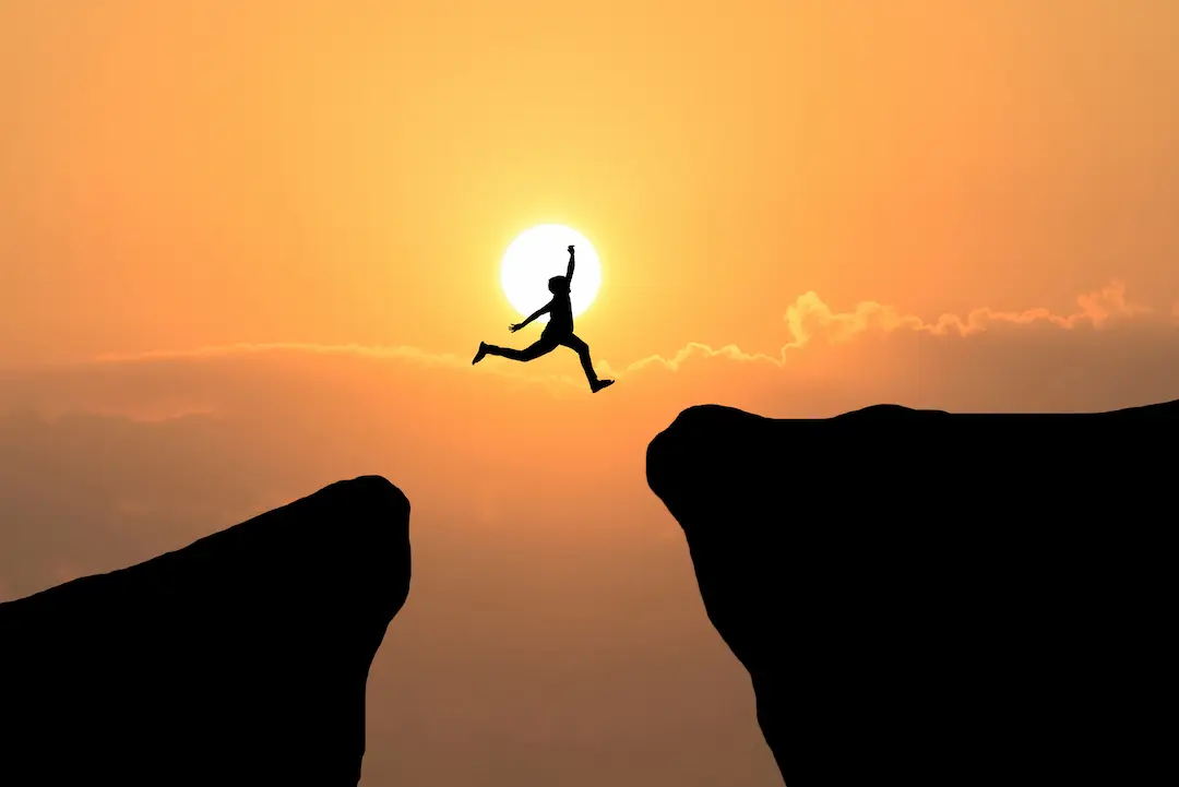 Homme qui saute d'une montagne à une autre sur un fond de coucher de soleil, libre